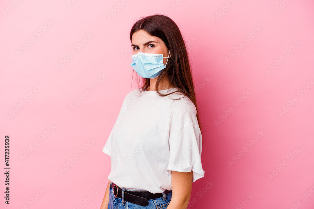 Young caucasian woman wearing a mask for virus isolated on pink background looks aside smiling, cheerful and pleasant. Young caucasian woman wearing a mask for virus isolated on pink background looks aside smiling, cheerful and pleasant.