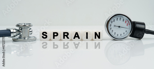 On a reflective white surface lies a stethoscope and cubes with the inscription - SPRAIN