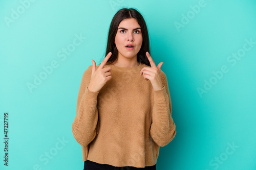 Young caucasian woman isolated on blue background pointing upside with opened mouth.