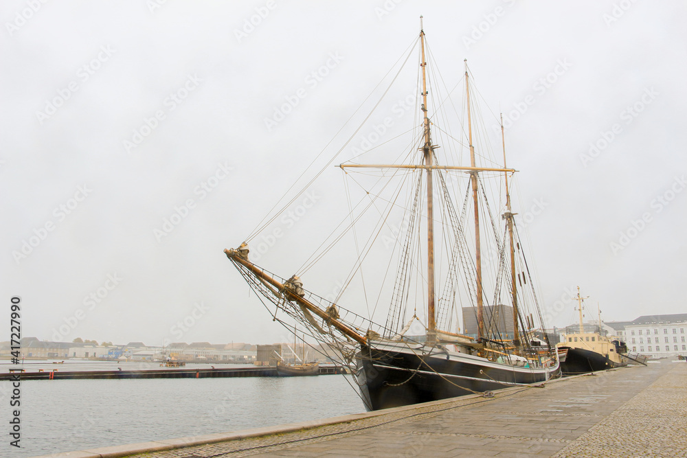 Obraz premium sailing ship with lowered sails moored on the embankment in rainy weather