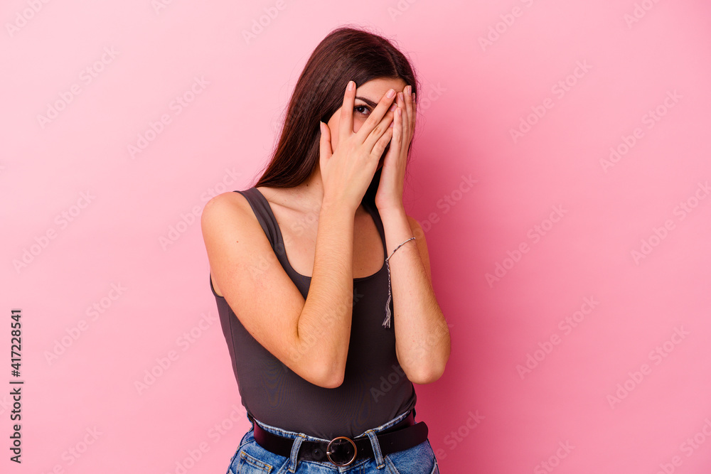 Young caucasian woman isolated on pink background blink through fingers frightened and nervous. Young caucasian woman isolated on pink background blink through fingers frightened and nervous.