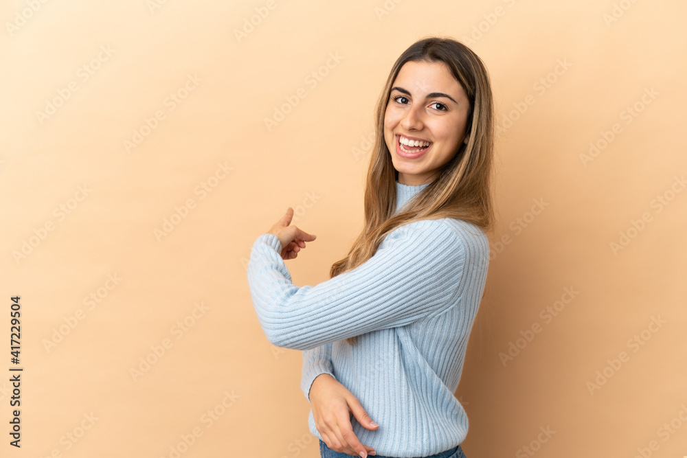 Obraz premium Young caucasian woman isolated on beige background pointing back