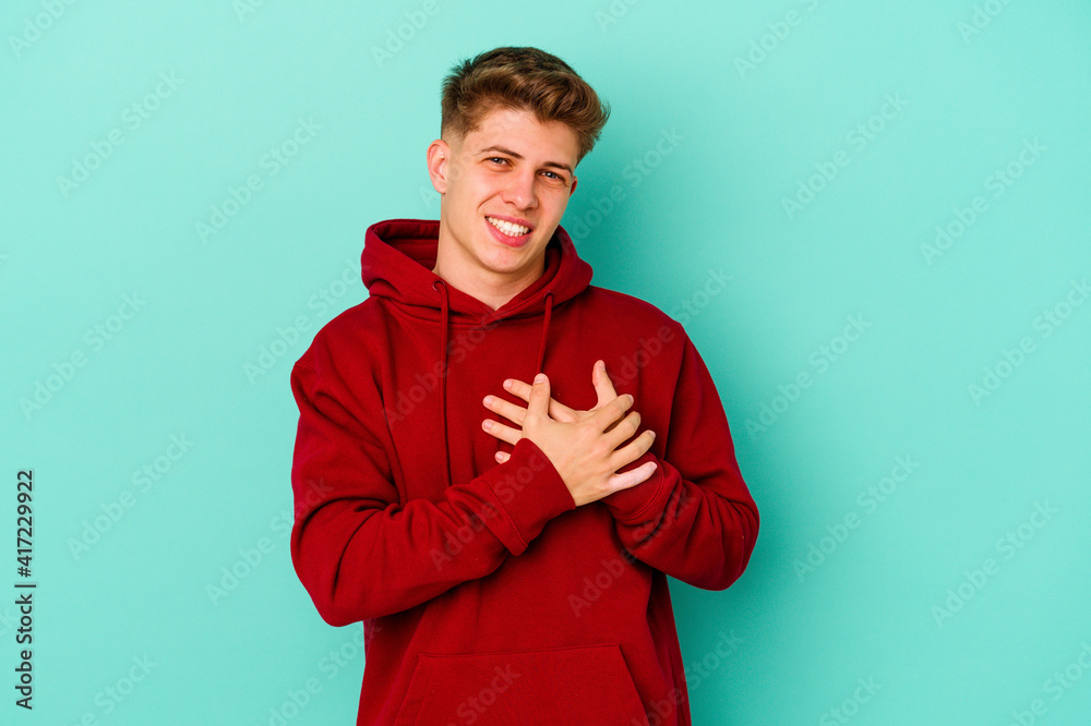 Young caucasian man isolated on blue background laughing keeping hands on heart, concept of happiness.