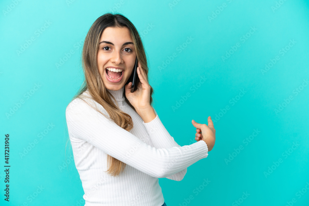 Fototapeta premium Young caucasian woman using mobile phone isolated on blue background pointing back