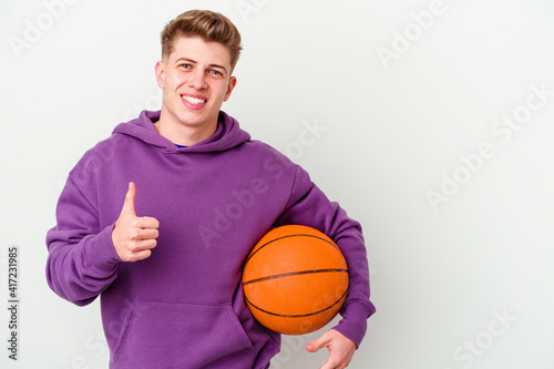 Young caucasian man playing basketball isolated background smiling and raising thumb up