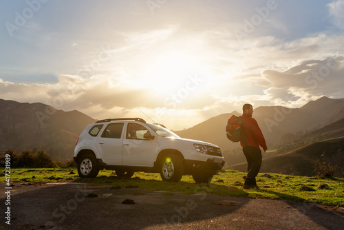 Fototapeta Naklejka Na Ścianę i Meble -  Hiker with backpack watches the sunset on the mountain with his all-terrain car. suv vehicle. Adventure and hiking