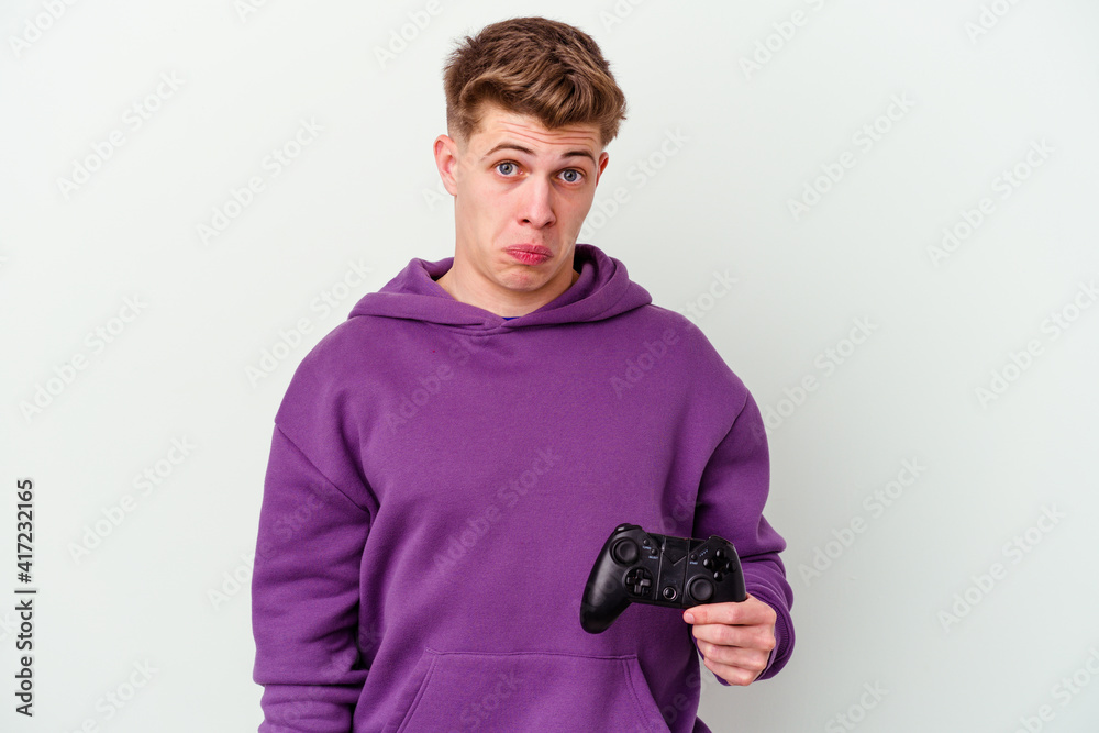 Young caucasian man holding a gamepad isolated on white background shrugs shoulders and open eyes confused. Young caucasian man holding a gamepad isolated on white background shrugs shoulders and open eyes confused.