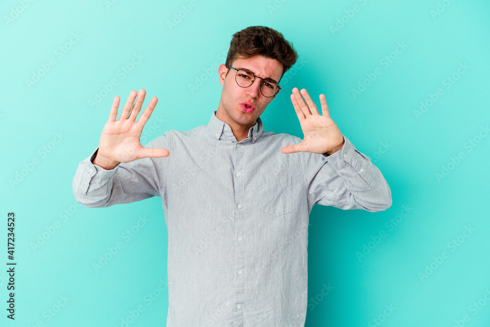 Young caucasian man isolated on blue background rejecting someone showing a gesture of disgust. Young caucasian man isolated on blue background rejecting someone showing a gesture of disgust.