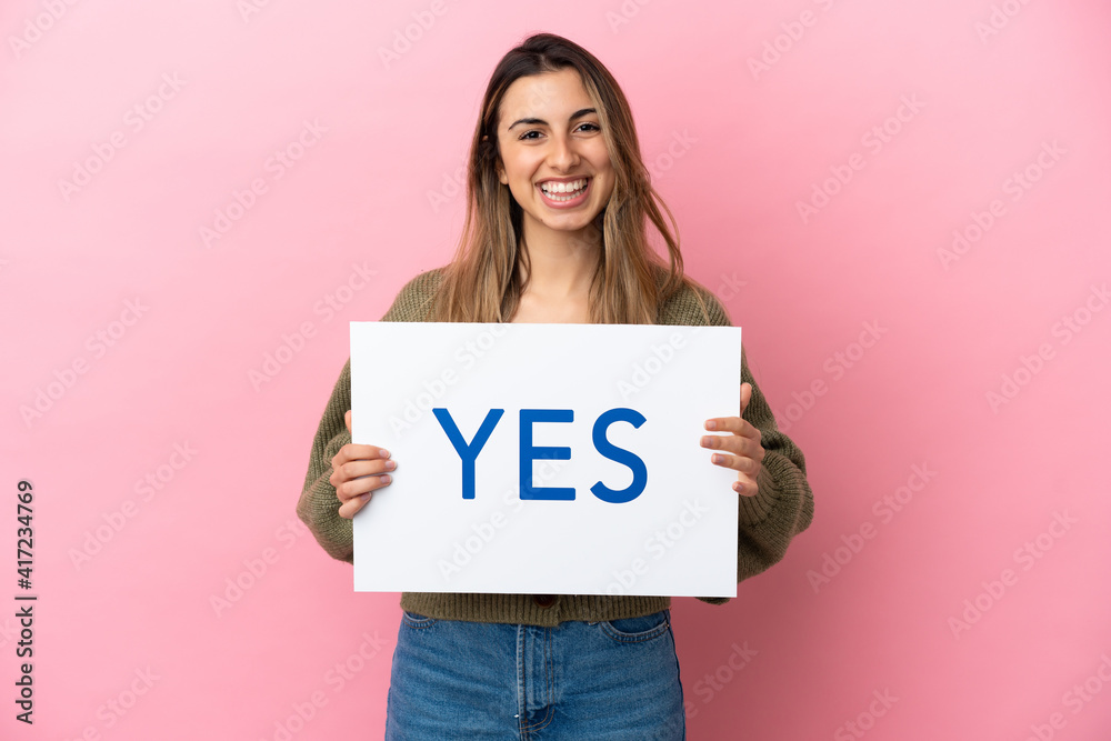 Young caucasian woman isolated on pink background holding a placard with text YES with happy expression Young caucasian woman isolated on pink background holding a placard with text YES with happy expression