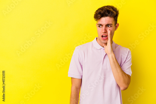 Young caucasian man isolated on yellow background is saying a secret hot braking news and looking aside
