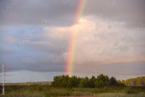 Double rainbow on a gray sky after rain. A rare atmospheric phenomenon after a storm. Beautiful hilly landscape with a real rainbow after rain on a summer day.