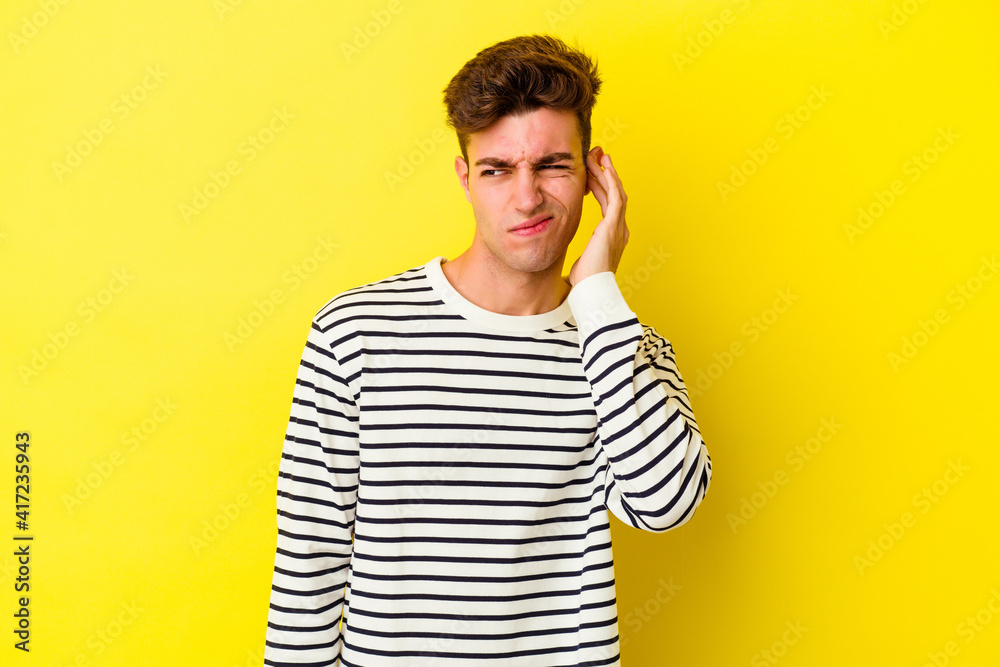 Young caucasian man isolated on yellow background covering ears with fingers, stressed and desperate by a loudly ambient. Young caucasian man isolated on yellow background covering ears with fingers, stressed and desperate by a loudly ambient.