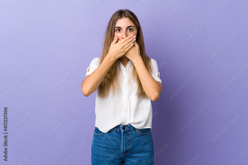 Young woman over isolated purple background covering mouth with hands Young woman over isolated purple background covering mouth with hands