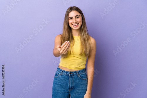 Young woman over isolated purple background inviting to come with hand. Happy that you came
