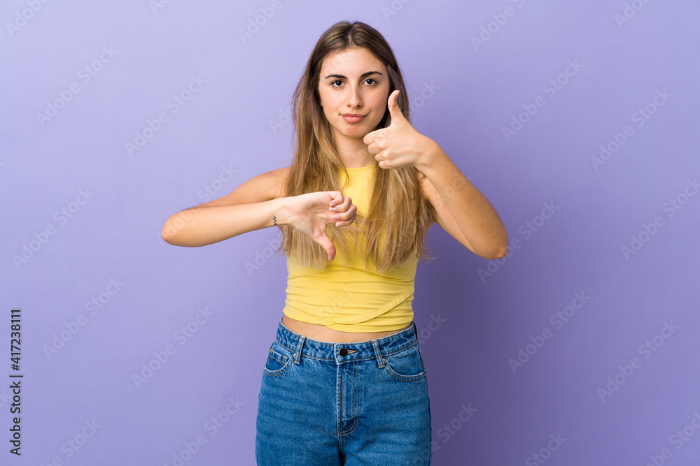 Young woman over isolated purple background making good-bad sign. Undecided between yes or not Young woman over isolated purple background making good-bad sign. Undecided between yes or not