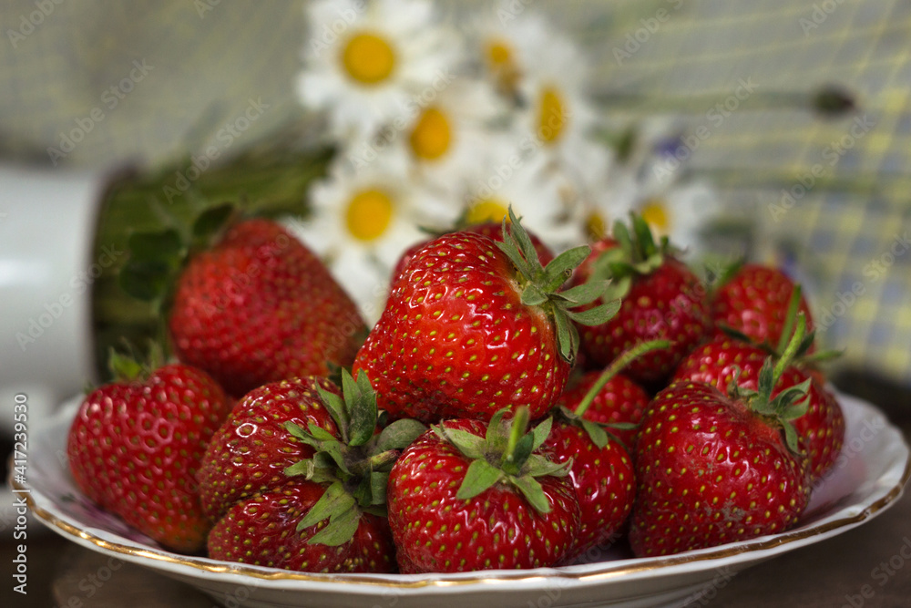 Ripe strawberries in a white old plate, near a rose. Brown wooden background Ripe strawberries in a white old plate, near a rose. Brown wooden background