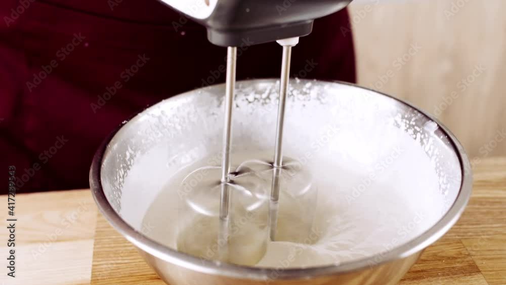 Male chefs hands whipping the egg protein in the metal using the mixer and adding ingredients like sugar, starch, salt, species