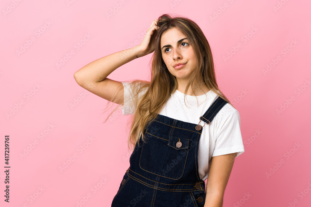Young woman over isolated pink background having doubts while scratching head Young woman over isolated pink background having doubts while scratching head