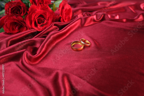 texture of luxury red silk fabric, background with waves and drapery for fashion design, gold wedding rings. bouquet of roses, concept of congratulations on wedding day