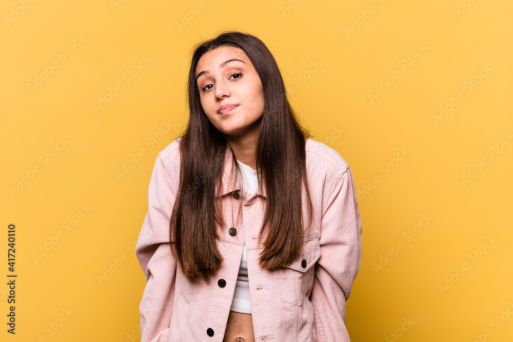 Young Indian woman isolated on yellow background shrugs shoulders and open eyes confused. Young Indian woman isolated on yellow background shrugs shoulders and open eyes confused.