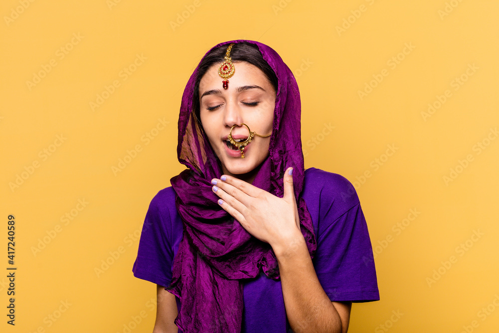 Young Indian woman wearing a traditional sari clothes isolated on yellow background laughs out loudly keeping hand on chest. Young Indian woman wearing a traditional sari clothes isolated on yellow background laughs out loudly keeping hand on chest.