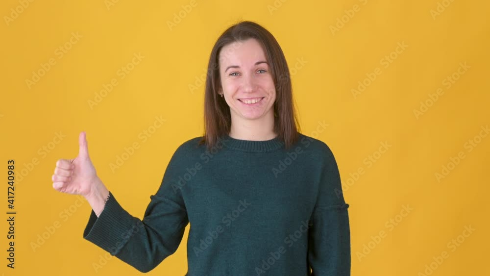 Positive young girl posing isolated on yellow studio background. Woman Looking approvingly at camera showing thumbs up, like sign positive something good. People lifestyle concept.