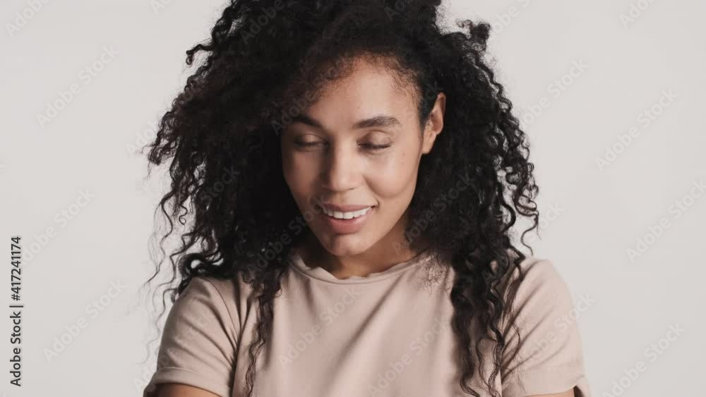 Young flirty African American woman with dark fluffy hair looking cute charmingly posing on camera over white background 