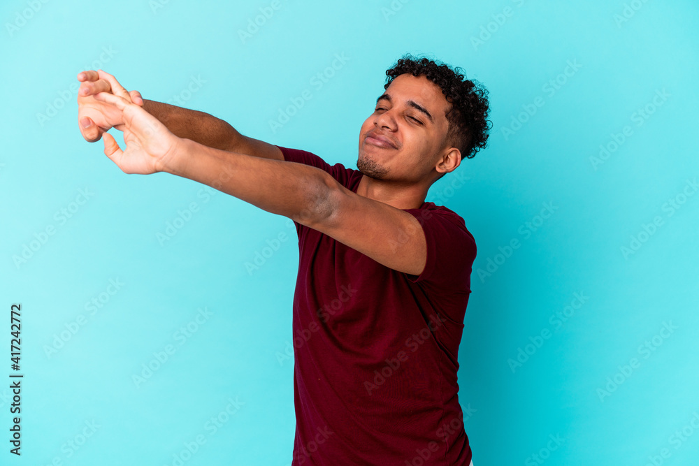 Young african american curly man isolated on blue stretching arms, relaxed position. Young african american curly man isolated on blue stretching arms, relaxed position.