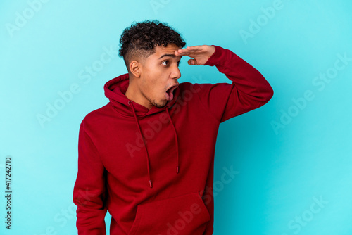 Young african american curly man isolated on blue looking far away keeping hand on forehead.