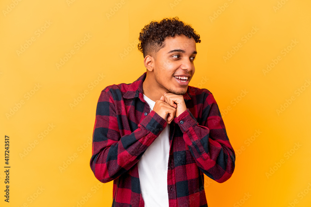 Young african american curly man isolated on purple keeps hands under chin, is looking happily aside. Young african american curly man isolated on purple keeps hands under chin, is looking happily aside.