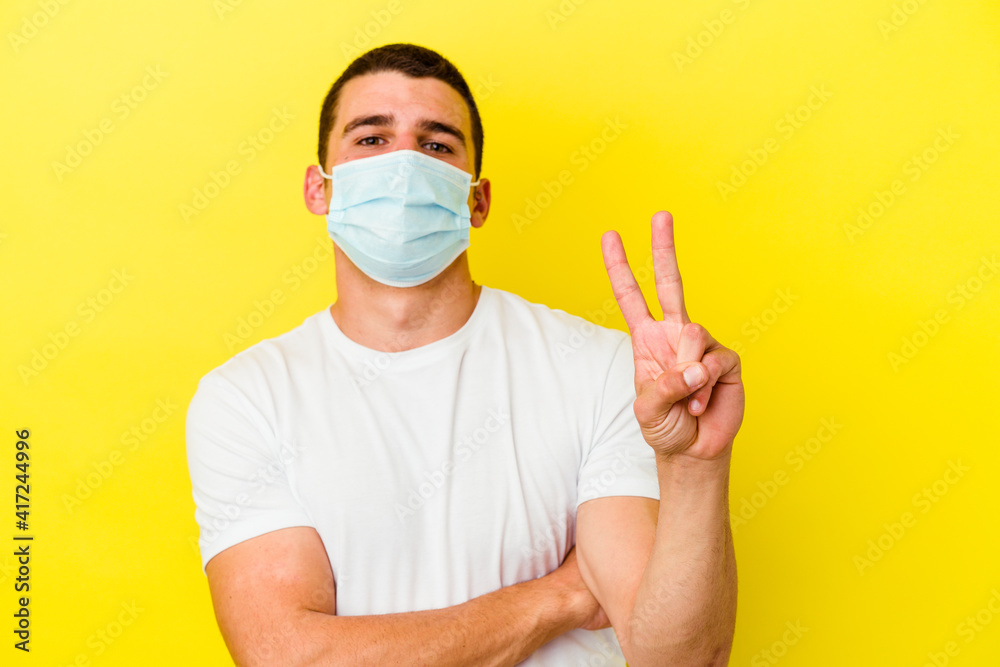 Young caucasian man wearing a protection for coronavirus isolated on yellow background showing number two with fingers. Young caucasian man wearing a protection for coronavirus isolated on yellow background showing number two with fingers.