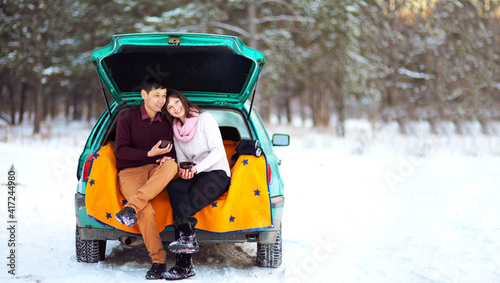 Happy couple sitting in the open trunk of a car in winter on nature