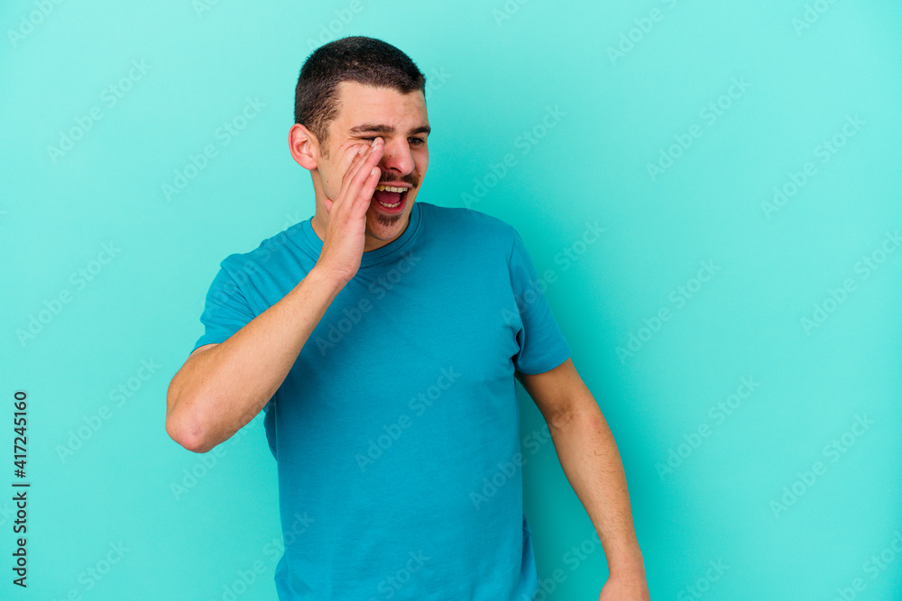 Young caucasian man isolated on blue background shouting excited to front.