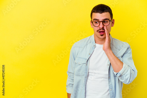 Young caucasian cool man isolated on yellow background is saying a secret hot braking news and looking aside