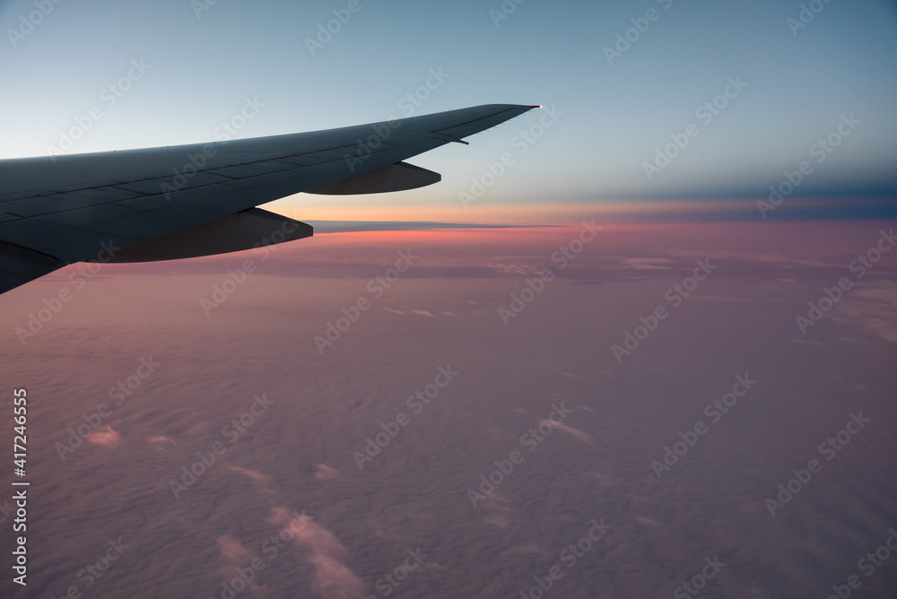 Aerial View from an Airplane. Flying above Clouds at Pink Sunrise
