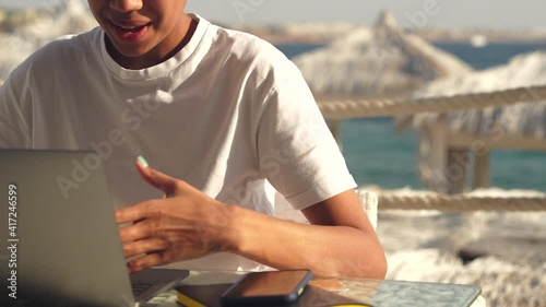 Explaination. Close up of young woman conducting business negotiations, conference, online learning, interview using her laptop while sitting on the beach on a sunny day. Freelancer, vacation concept