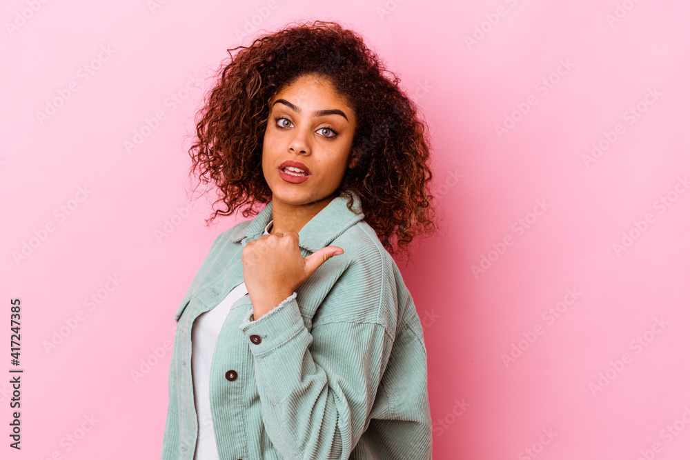 Young african american woman isolated on pink background points with thumb finger away, laughing and carefree. Young african american woman isolated on pink background points with thumb finger away, laughing and carefree.