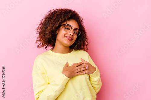 Young african american woman isolated on pink background has friendly expression, pressing palm to chest. Love concept.