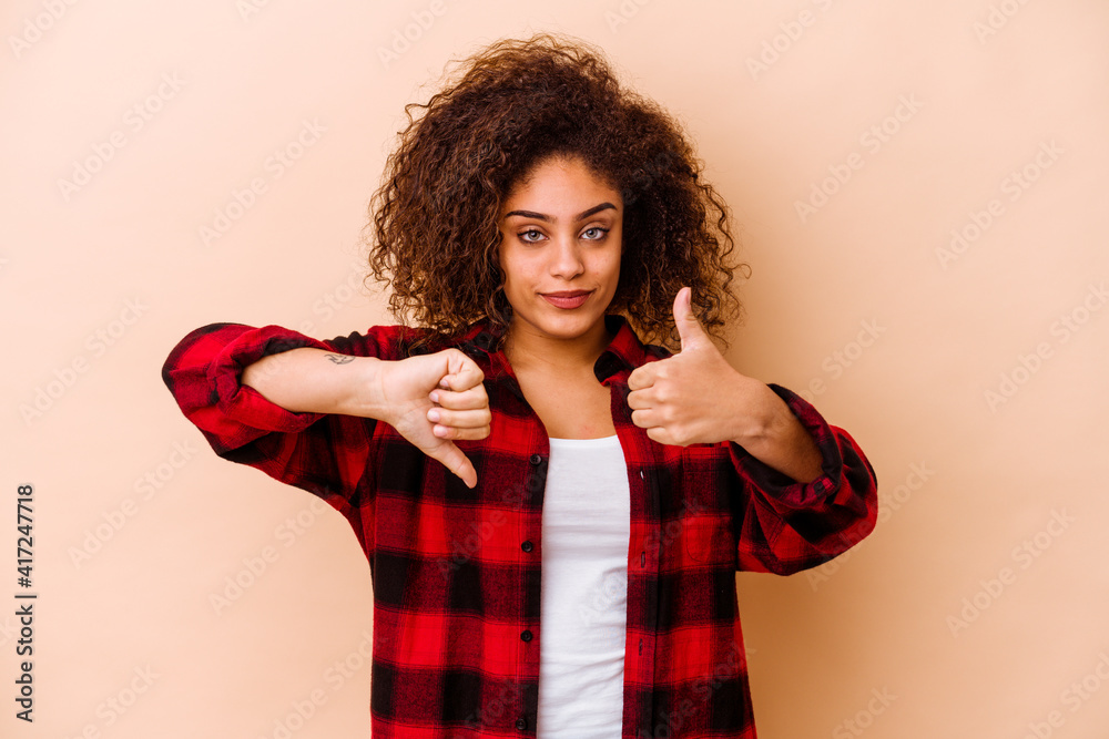 Young african american woman isolated on beige background showing thumbs up and thumbs down, difficult choose concept Young african american woman isolated on beige background showing thumbs up and thumbs down, difficult choose concept