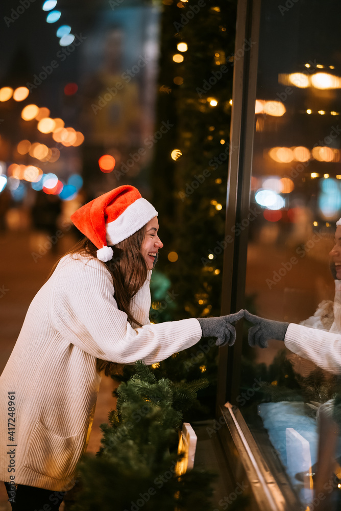 Smiling girl looking through shop window, city lights on background. Smiling girl looking through shop window, city lights on background.