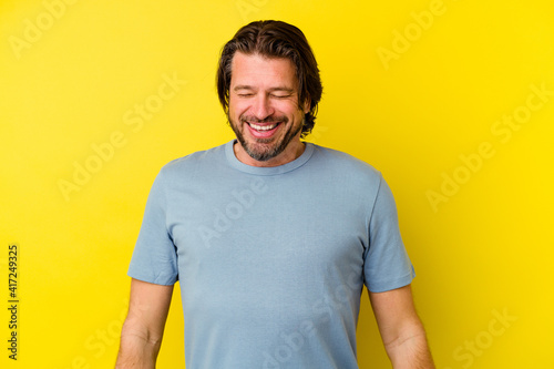 Middle age caucasian man isolated on yellow background laughs and closes eyes, feels relaxed and happy.