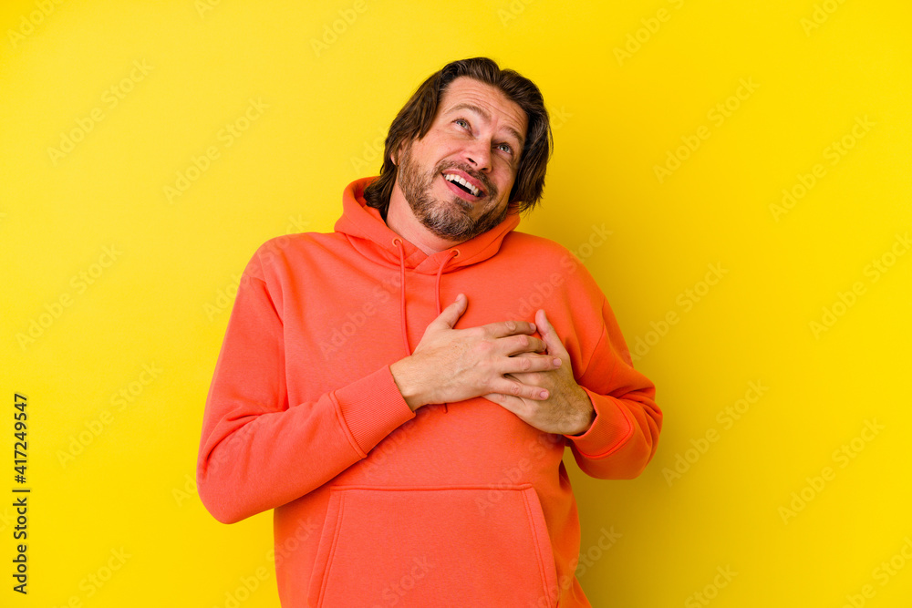 Middle age caucasian man isolated on yellow background laughing keeping hands on heart, concept of happiness.