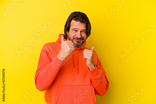 Middle age caucasian man isolated on yellow background raising both thumbs up, smiling and confident.