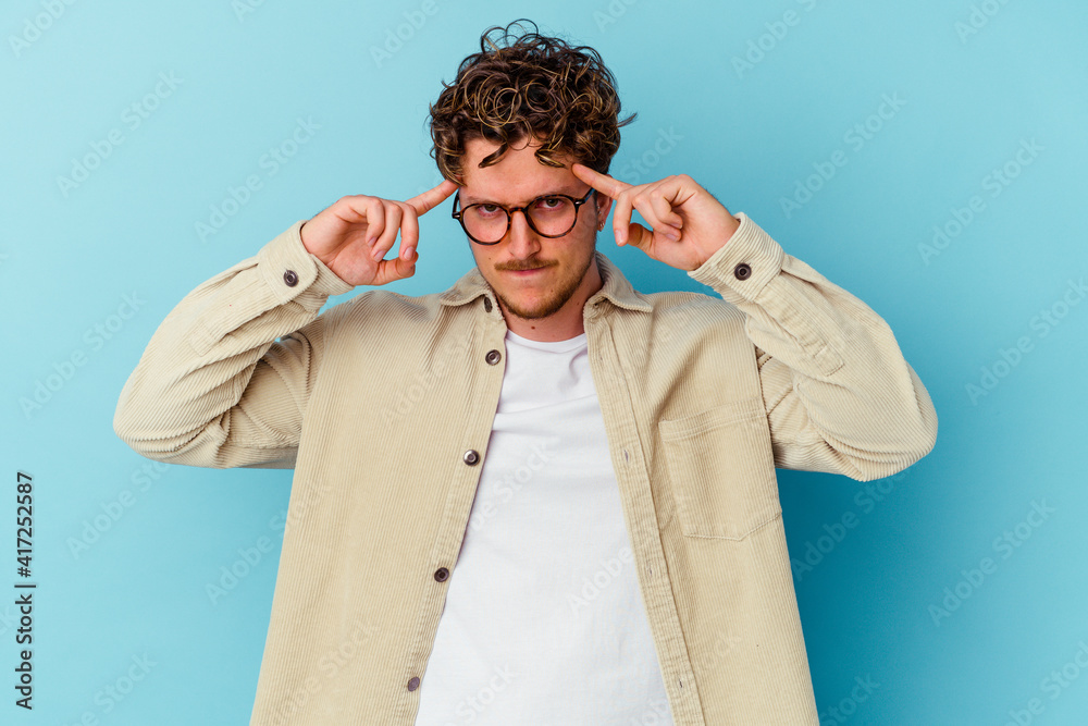 Young caucasian man wearing eyeglasses isolated on blue background focused on a task, keeping forefingers pointing head. Young caucasian man wearing eyeglasses isolated on blue background focused on a task, keeping forefingers pointing head.