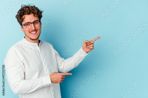 Young caucasian business man isolated on blue background excited pointing with forefingers away.