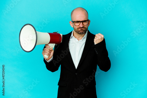 Young business bald man holding a megaphone isolated showing fist to camera, aggressive facial expression.