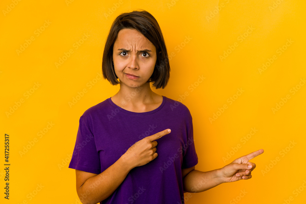 Young hispanic woman isolated on yellow shocked pointing with index fingers to a copy space. Young hispanic woman isolated on yellow shocked pointing with index fingers to a copy space.