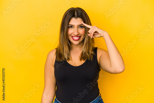 Young indian woman isolated on yellow background pointing temple with finger, thinking, focused on a task.