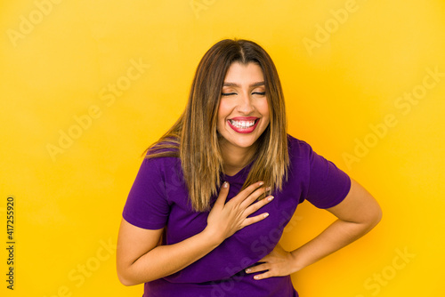 Young indian woman isolated on yellow background laughing keeping hands on heart, concept of happiness.