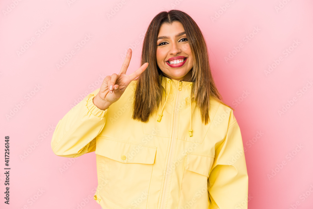 Young indian woman isolated on pink background joyful and carefree showing a peace symbol with fingers. Young indian woman isolated on pink background joyful and carefree showing a peace symbol with fingers.